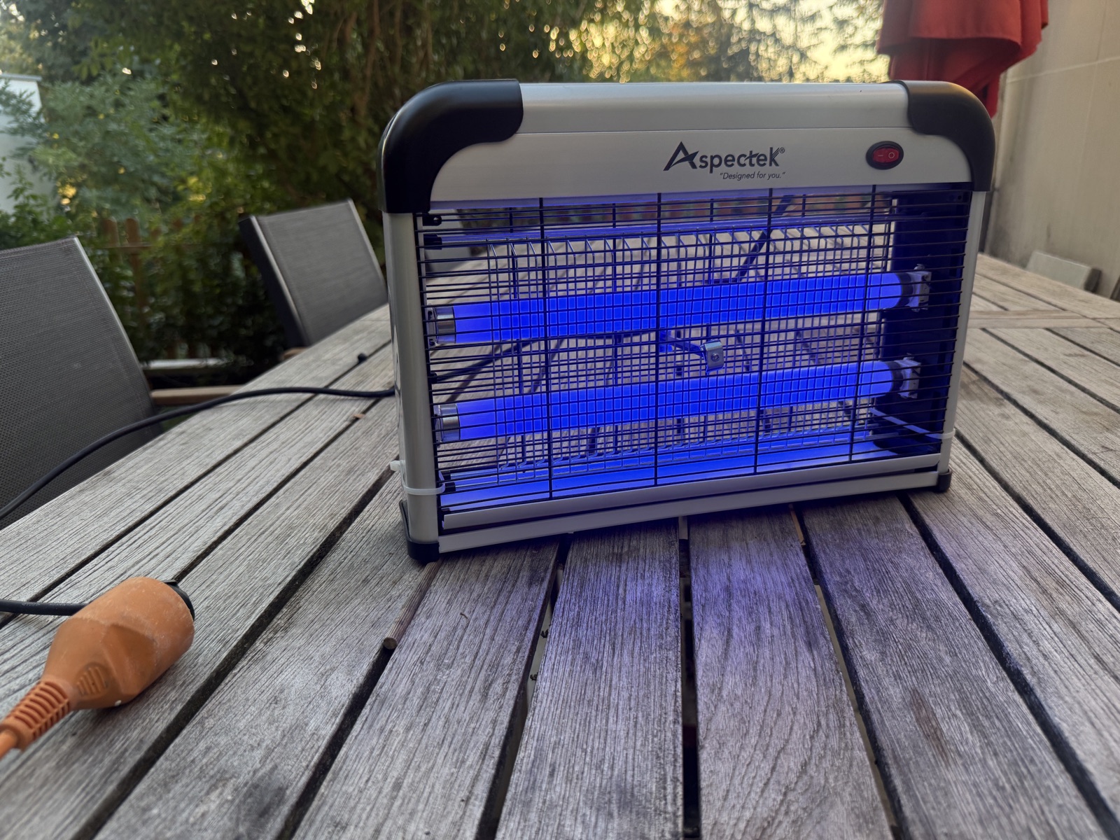Le tue-insectes Aspectek 20 W posé sur notre table de jardin en teck au crépuscule, tubes UV allumés, avec sa rallonge orange au premier plan