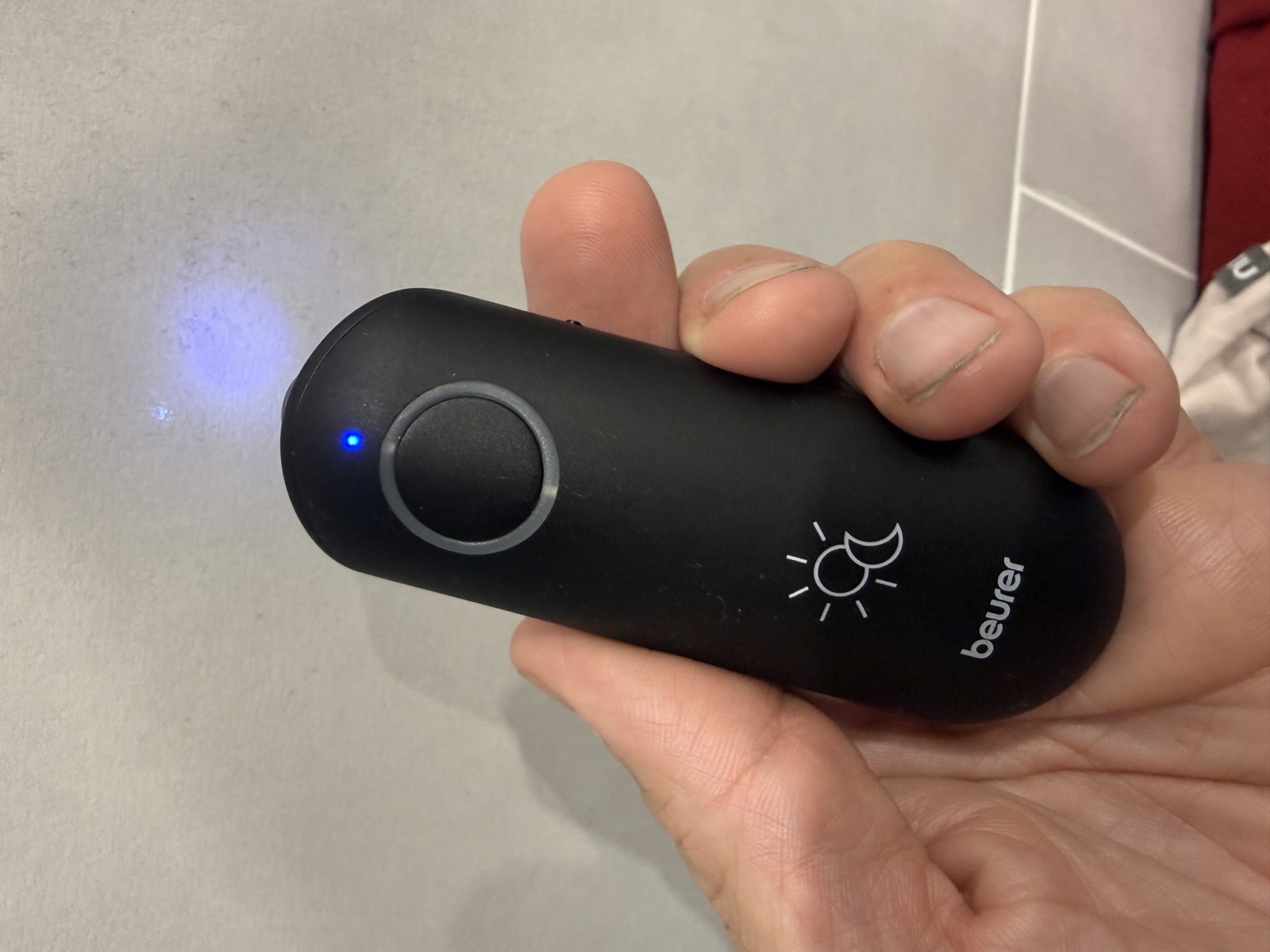 Le stylo chauffant Beurer BiteX Day&Night noir tenu en main, LED bleue de fonctionnement allumée, pictogrammes jour et nuit visibles