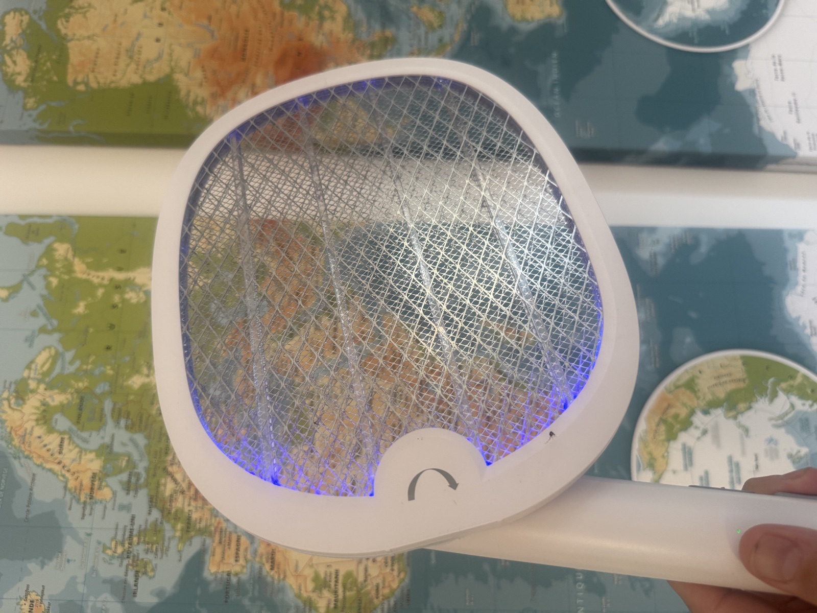La raquette YISSVIC pli&eacute;e &agrave; 90&deg; tenue par le manche dans une chambre d'enfant au papier peint carte du monde, en position lampe pos&eacute;e