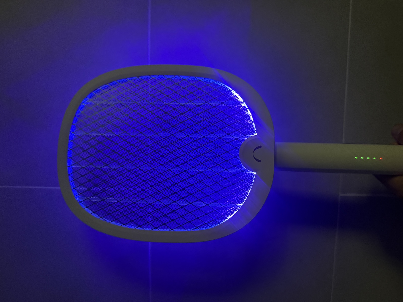 La raquette YISSVIC de nuit dans la salle de bain, grille enti&egrave;rement &eacute;clair&eacute;e en violet, quatre LED vertes de charge et LED rouge d'armement visibles sur le manche